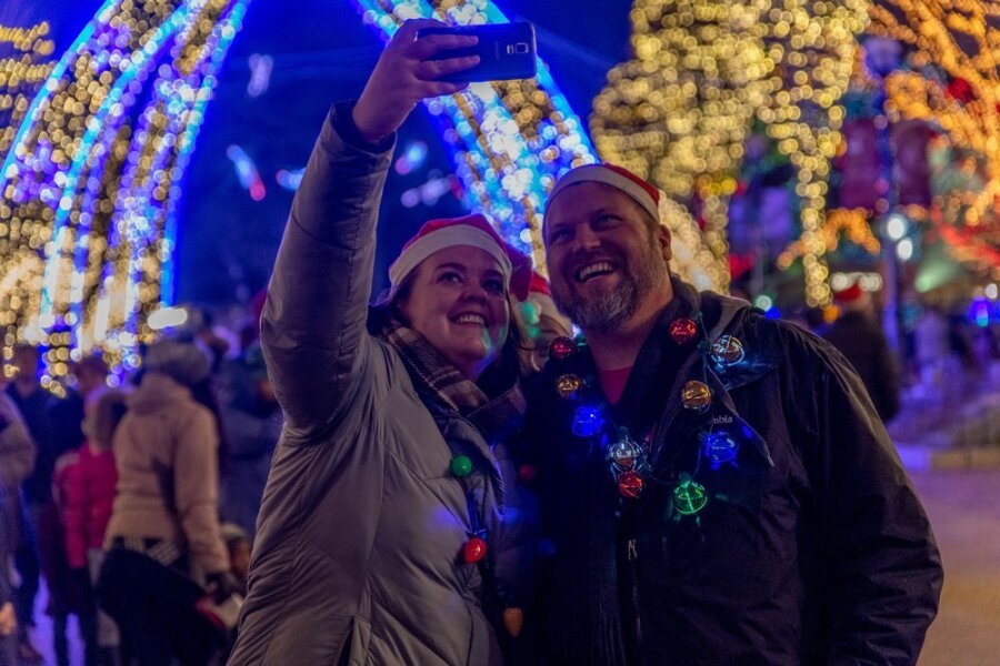 Couple in Santa hats taking a selfie surrounded by glowing holiday light arches